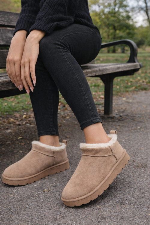 Person wearing beige ankle boots with fur trim sitting on a bench outdoors.
