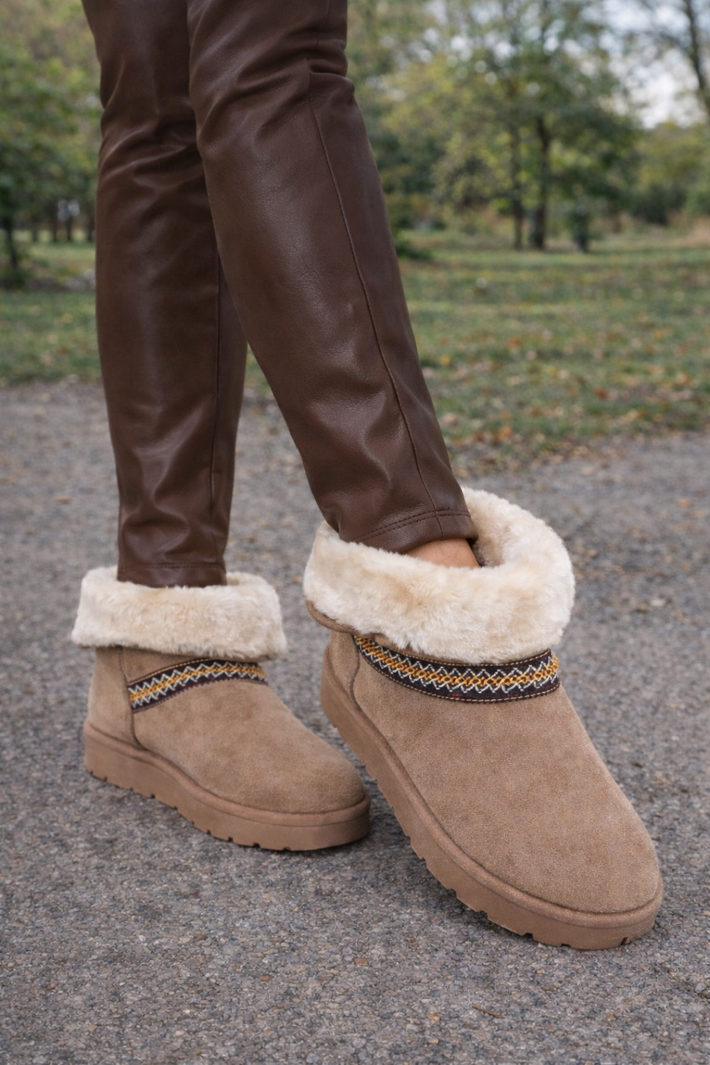 Brown suede boots with fur trim worn outdoors on a gravel path.
