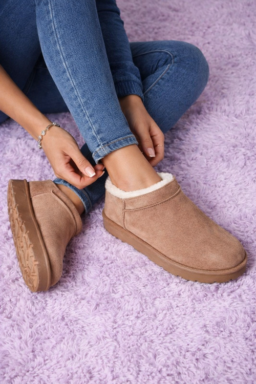 Person wearing brown suede clog shoes with white fur lining on a purple textured surface.