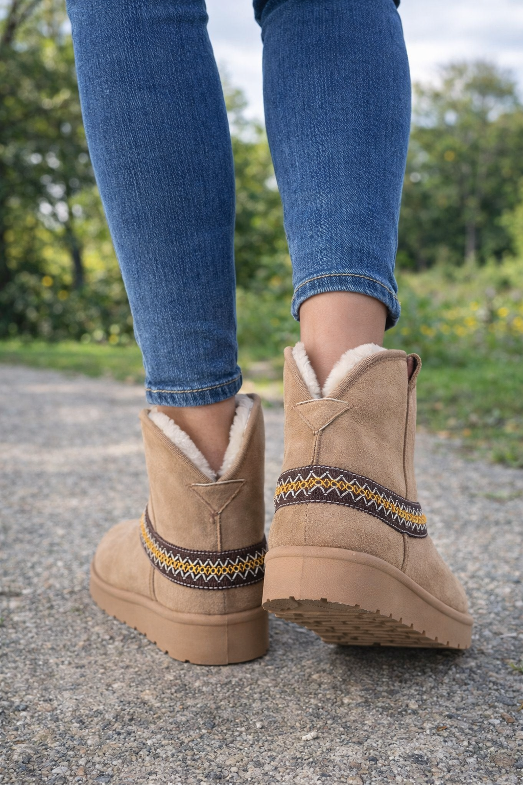 Tan winter boots with decorative patterns worn with blue jeans on a blurred natural background