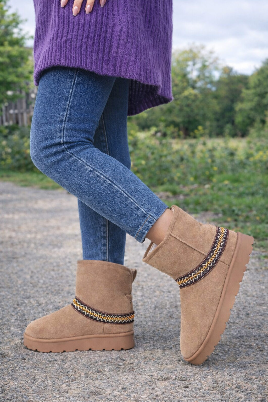 Person wearing brown suede boots with decorative straps on a blurred outdoor background