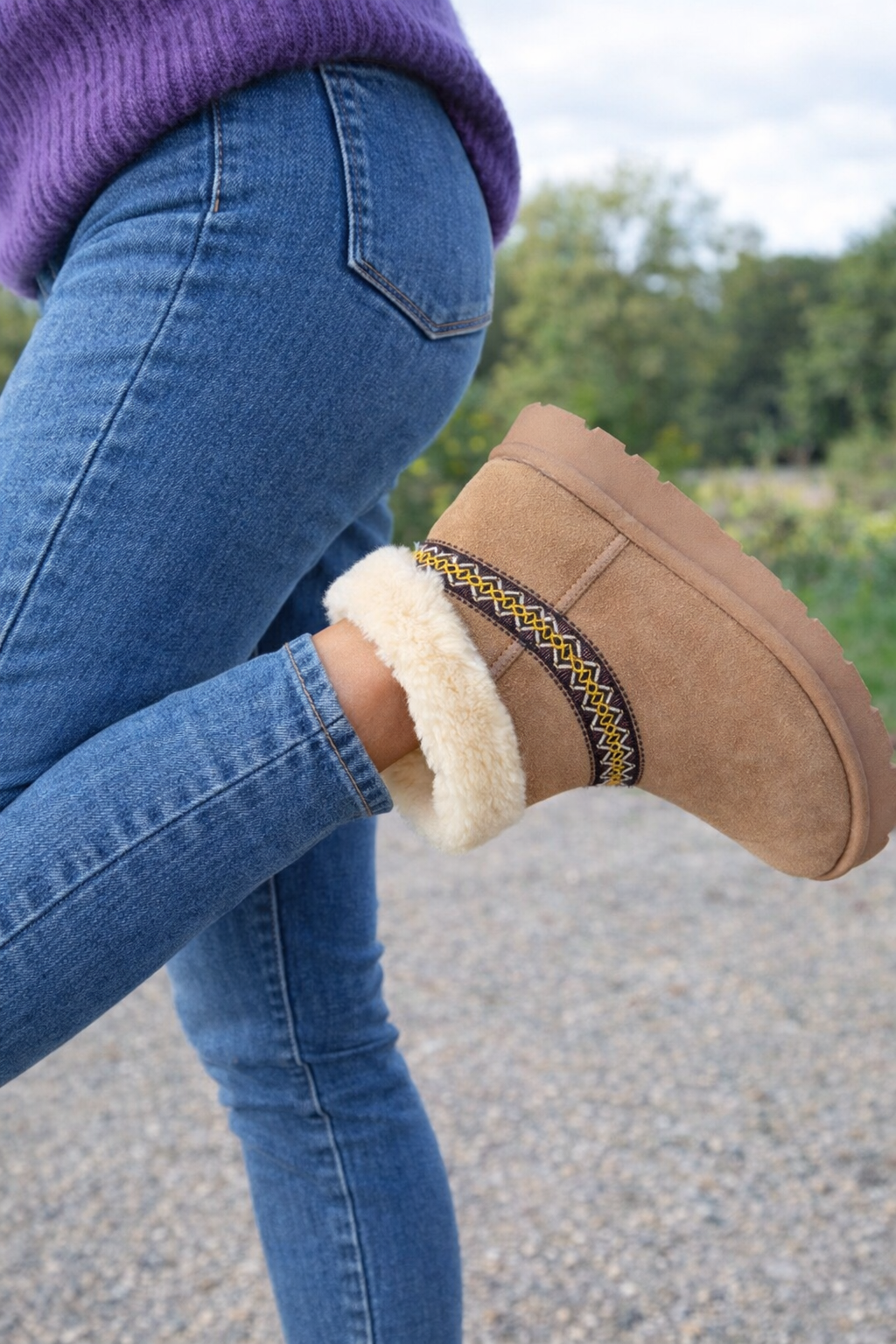 Brown suede boot with shearling lining worn by a person in blue jeans outdoors.