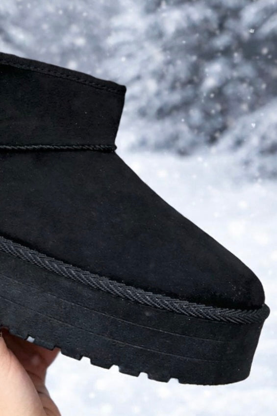 Black snow boot with a textured sole held against a snowy background